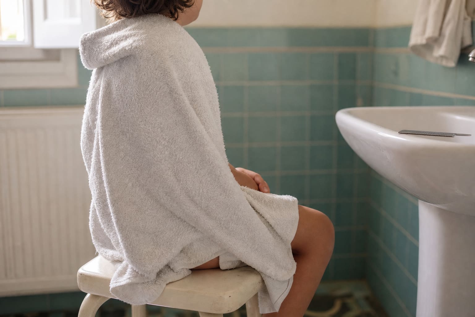 Enfant assis sur un tabouret de salle de bains, une serviette sur les épaules, lumière douce