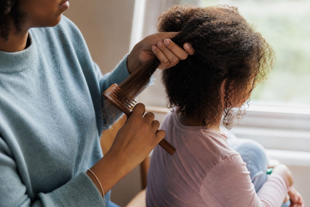 Parent démêlant avec soin une chevelure crépue près d'une fenêtre, lumière naturelle douce